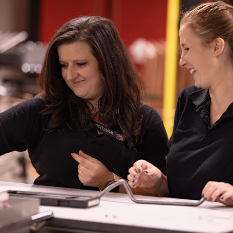 Två medarbetare står leendes och granskar en bockad trådprodukt