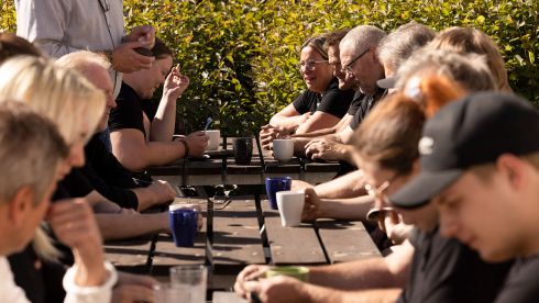 Ett gäng medarbetare sitter utomhus i solen och dricker kaffe