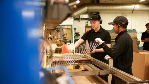 Två medarbetare hjälps åt att lyfta upp ett galler från en maskin