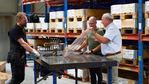 Personer i teamet står vid ett bord och diskuterar ett gallerskydd som tillverkats