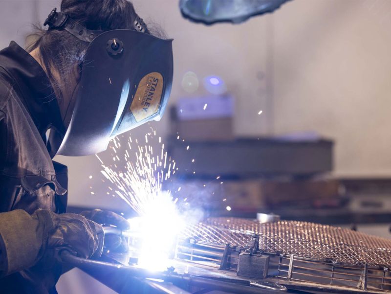 Medarbetare svetsar ett galler och gnistor flyger upp
