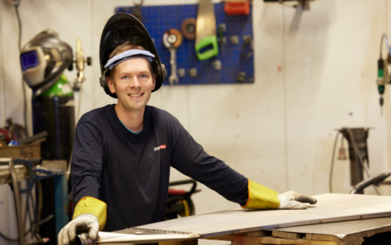 Leende medarbetare står med svetshjälm i produktion 
