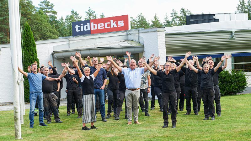 Hela teamet står med armarna upp i luften utanför Tidbecks kontor 
