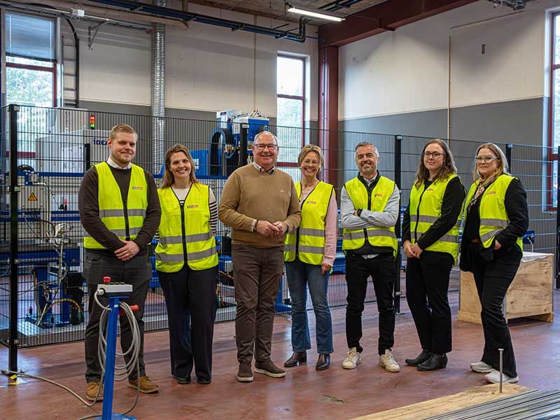 Personer står och tittar mot kameran framför en maskin på lagret