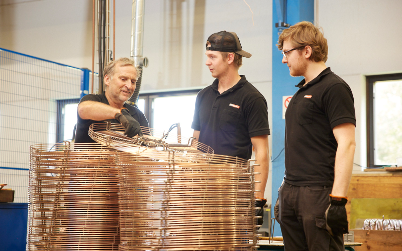 En medarbetare visar upp tillverkade fläktskydd för två andra medarbetare
