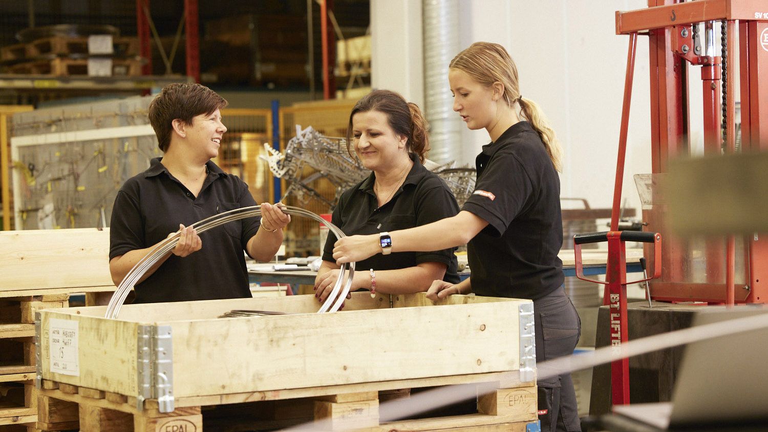 Tre medarbetare står runt en trälåda med metalltråd i
