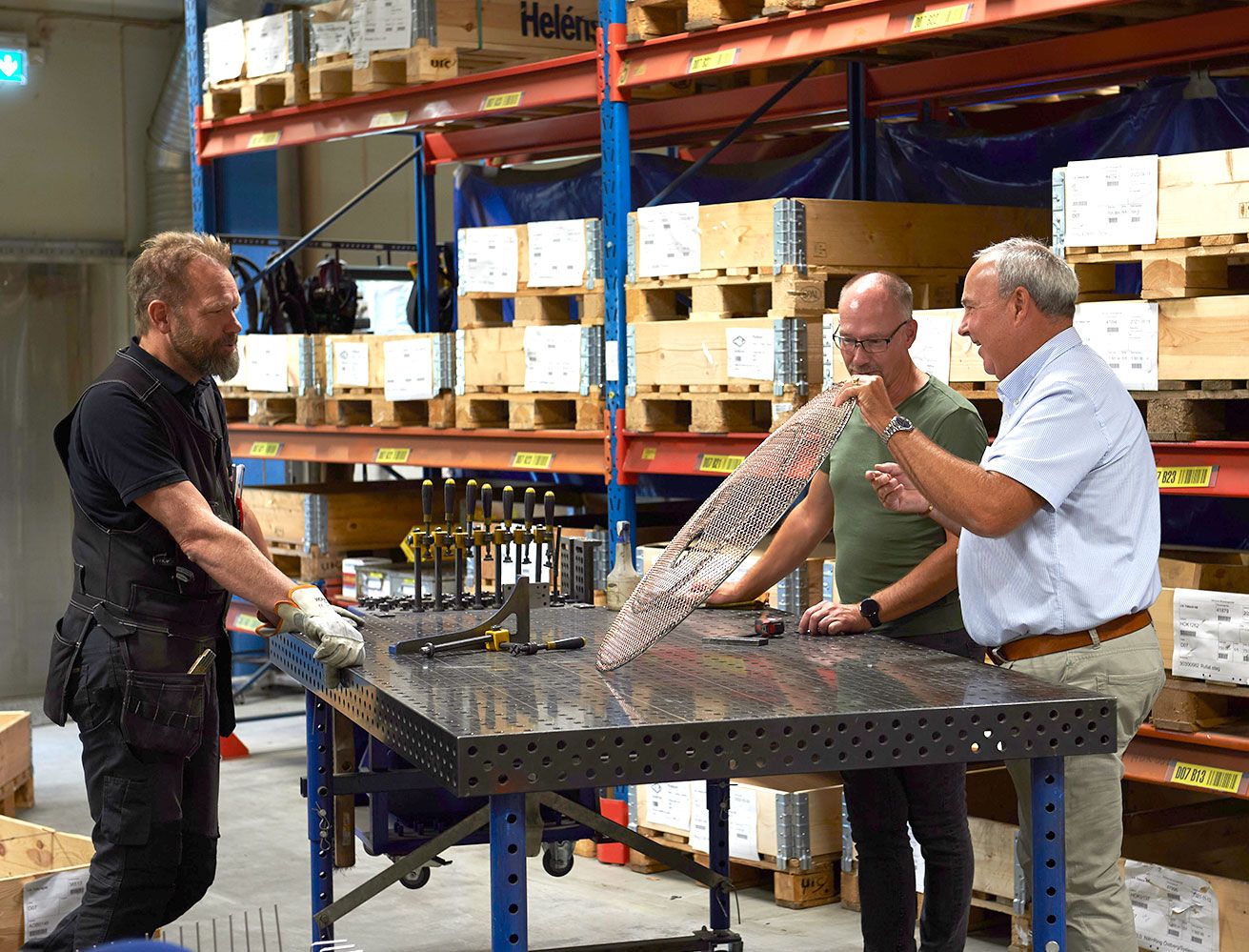 Tre personer på ett lager diskuterar och visar upp produkt