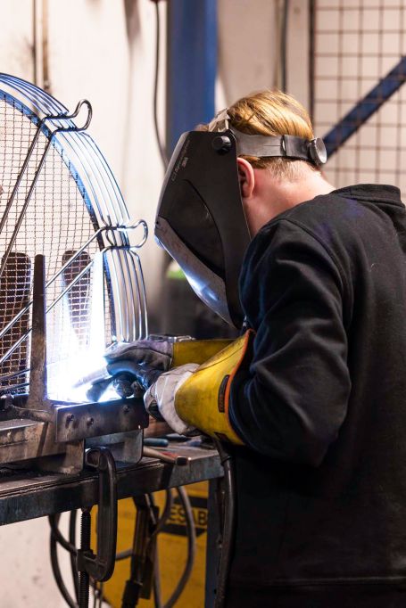 En lärling svetsar ett galler med en handledare som står bakom och överser svettsninge