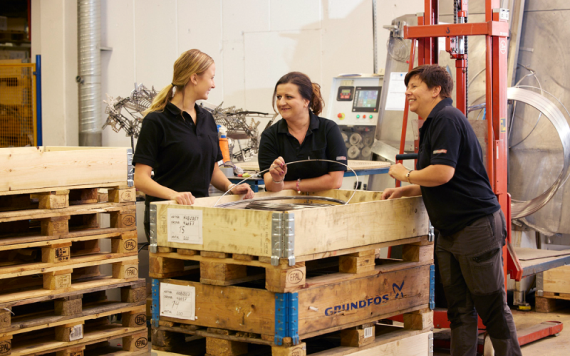 Medarbetare står och pratar vid pallar med metalltråd
