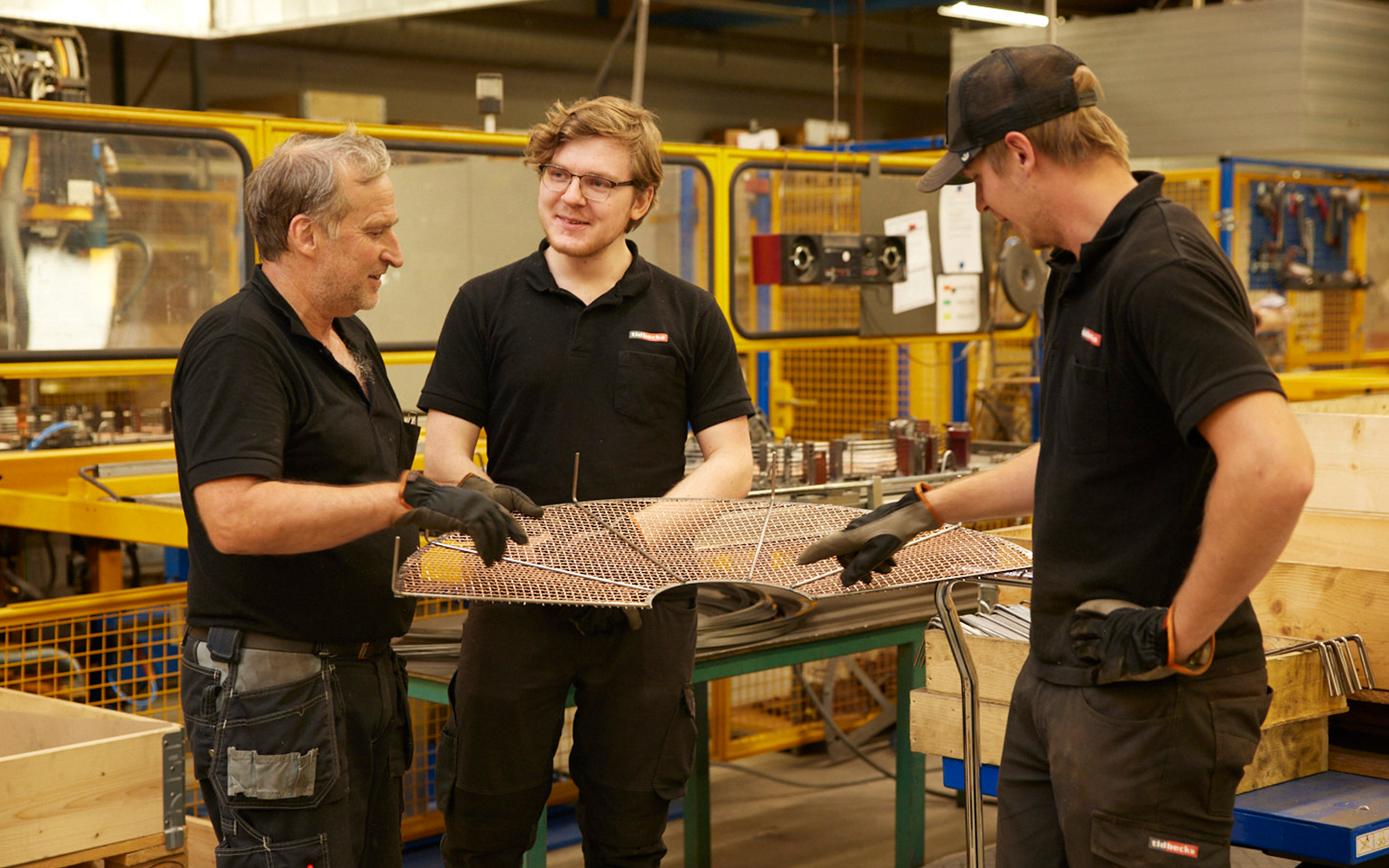 Tre medarbetare granskar och diskuterar ett krenelerat galler