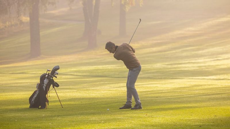 Person svingar sin klubba på en golfbana en solig och lite dimmig morgon